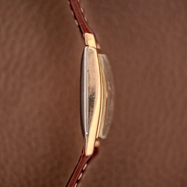 Close-up side view of the Hamilton Asymmetric Khyber Manual Wind Caliber 730 wristwatch with a brown leather strap, displayed against a textured brown background.