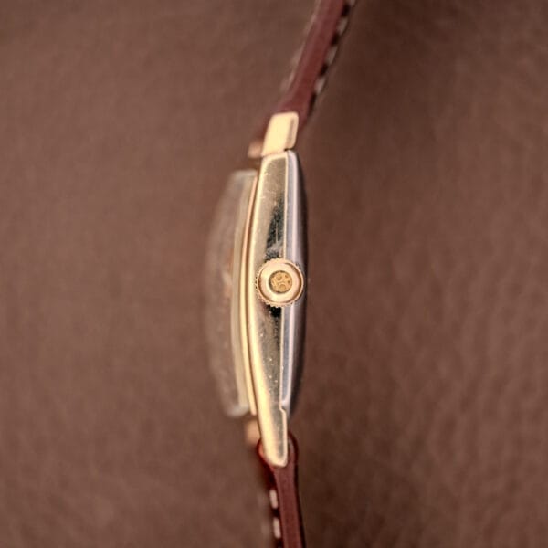 Side view of the Hamilton Asymmetric Khyber Manual Wind Caliber 730 in gold, featuring a brown leather strap, displayed on a textured brown surface.