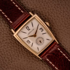 The Hamilton Asymmetric Khyber Manual Wind Caliber 730 wristwatch, with a rectangular face and brown leather strap, rests elegantly on a textured brown surface.