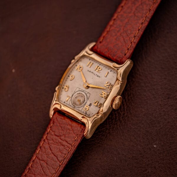 Hamilton Lawton Art Deco wristwatch with a gold filled case, manual wind Cal. 747 movement, and brown leather strap, shown on a dark brown leather surface.