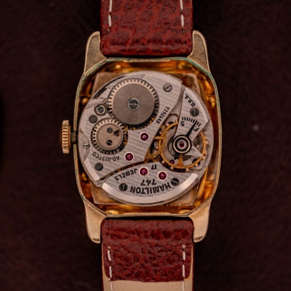 Close-up of the Hamilton Lawton Art Deco Gold Filled Case watch, showcasing its manual wind Cal. 747 movement with visible gears and a brown leather strap.