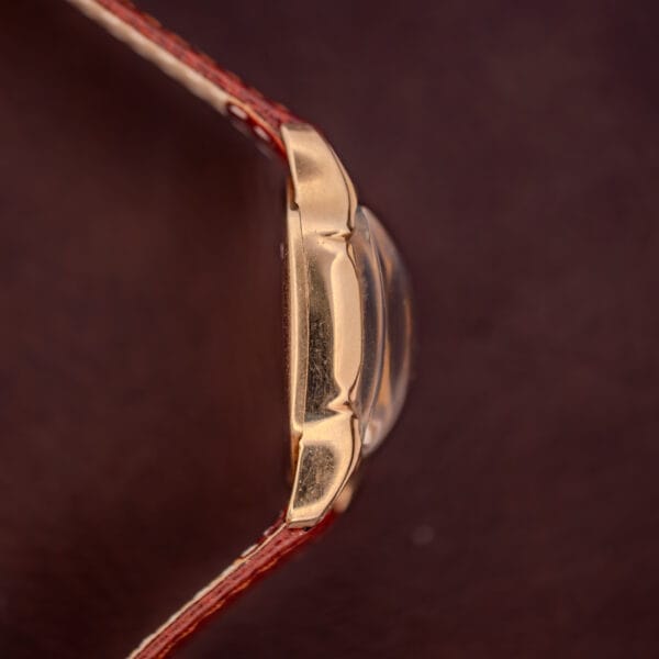 Close-up side view of a Hamilton Lawton Art Deco Gold Filled Case Manual Wind Cal. 747 wristwatch with a brown leather strap against a dark background.