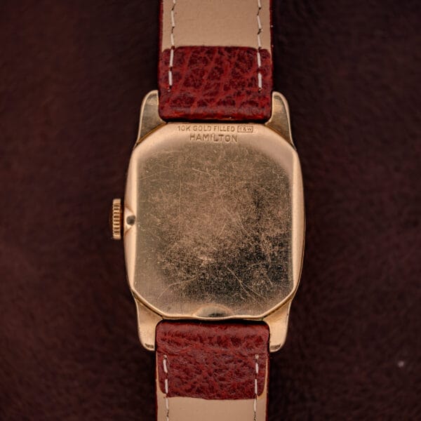 Back of a Hamilton Lawton Art Deco Gold Filled Case Manual Wind Cal. 747 wristwatch with red leather strap, displaying visible scratches on its gold filled Art Deco-inspired case.