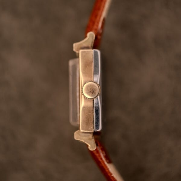 Side view of the Hamilton Art Deco Square Gold Filled Case Manual Wind Cal. 987-F wristwatch with a brown leather strap and prominent crown, set against a blurred background.