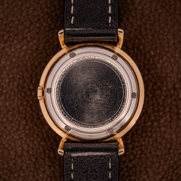 Close-up of a Hamilton K-454 Sputnik Automatic Cal. 661 watch’s scratched gold filled case back, black leather strap with visible stitching.