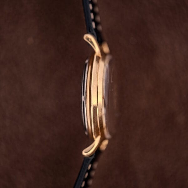 Side view of a Hamilton K-454 Sputnik Automatic Cal. 661 gold wristwatch with black strap and Gold Filled Case against a brown background.