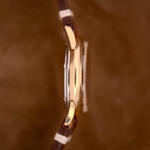 Side view of the Zodiac Hermetic Black Dial Automatic Caliber 1624 with a gold filled case and brown leather strap, displayed against a brown background.