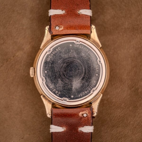 The back of a vintage Zodiac Hermetic Black Dial Automatic Caliber 1624 with a gold filled case and brown leather strap rests on suede, showcasing its timeless style.
