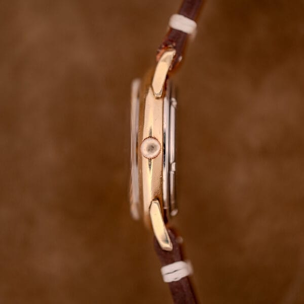 Side view of the Zodiac Hermetic Black Dial Automatic Caliber 1624 wristwatch in a gold filled case with a brown leather strap, set against a brown background.