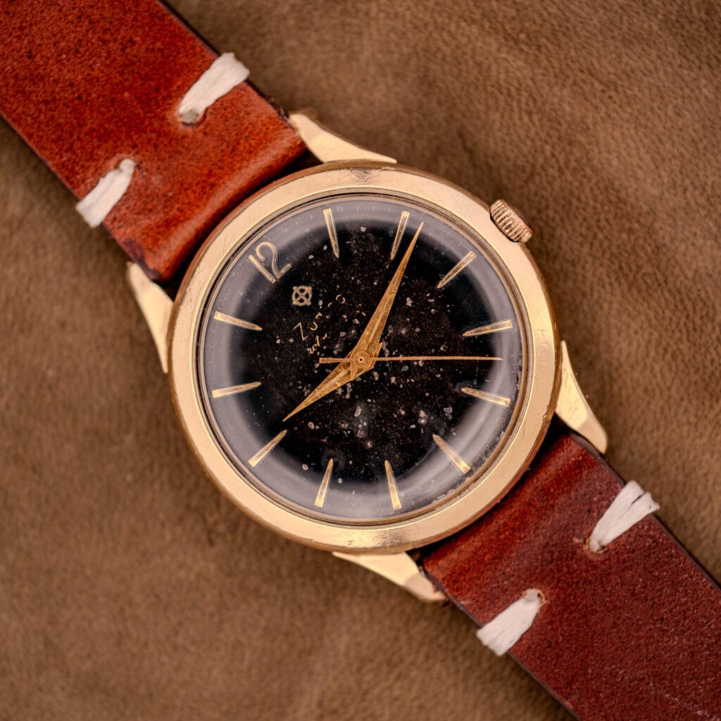 The Zodiac Hermetic Black Dial Automatic Caliber 1624 with a gold filled case rests elegantly on a tan suede surface.