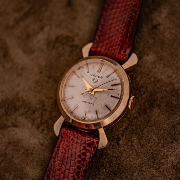 Gruen 21 Precision Manual Wind Fancy Lugs Ref. 335SS 723 wristwatch with brown textured leather strap, shown on brown suede; a vintage classic for timeless elegance.