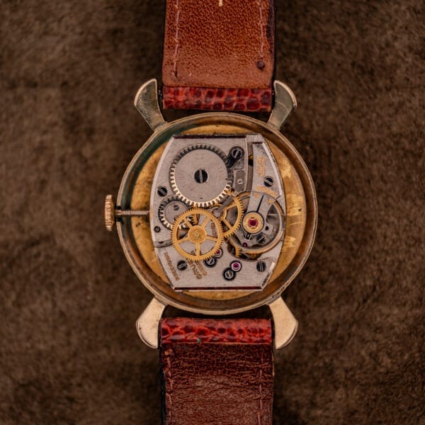 Close-up of a Gruen 21 Precision Manual Wind Fancy Lugs Ref. 335SS 723 vintage wristwatch, showcasing exposed gears and a brown leather strap.