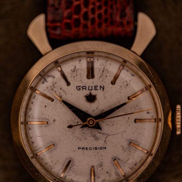 Gruen 21 Precision Manual Wind Fancy Lugs Ref. 335SS 723 wristwatch featuring a worn white dial, gold markers, fancy lugs, and a brown textured leather strap.