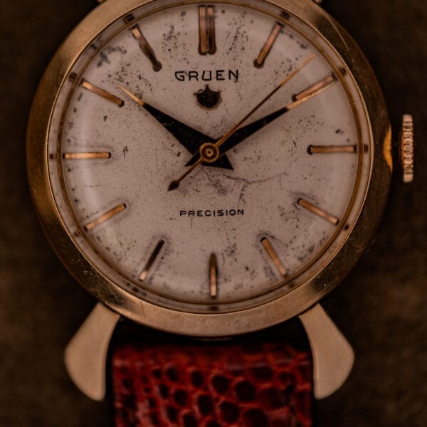 A vintage Gruen 21 Precision Manual Wind Fancy Lugs Ref. 335SS 723 wristwatch featuring a worn white dial and brown leather strap.