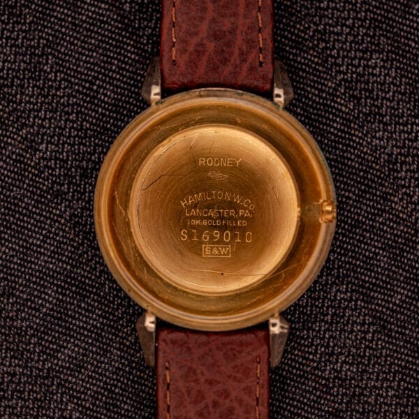 Hamilton Rodney Sector Dial Manual Wind Cal. 748 watch with a 10k gold filled case, engraved "RODNEY" on the back, brown leather strap, shown on dark fabric.
