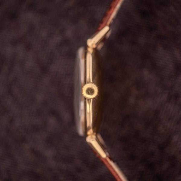 A close-up side view of the Hamilton Rodney Sector Dial Manual Wind Cal. 748, featuring a 10k gold filled case and brown leather strap, showcased against a textured background.