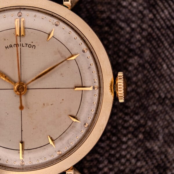 Close-up of a Hamilton Rodney Sector Dial Manual Wind wristwatch, Cal. 748, featuring simple hour markers and a 10k gold filled case, set on a textured dark background.