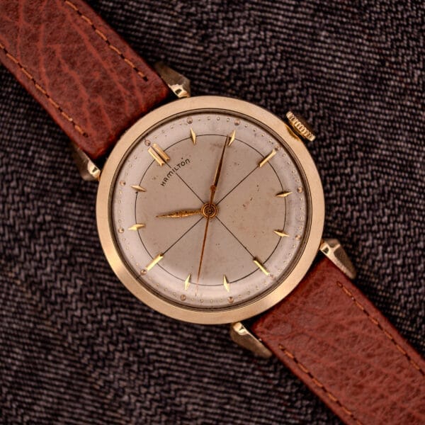 A Hamilton Rodney Sector Dial Manual Wind Cal. 748 with a 10k gold filled case and brown leather strap rests on textured dark fabric.