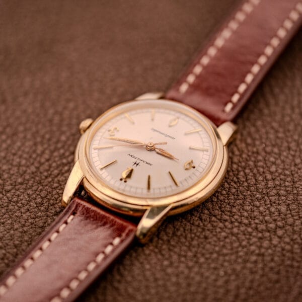 Hamilton Automatic Cal. 689 with a sunburst dial and 10k gold filled case, paired with a brown leather strap, displayed on a textured brown surface.