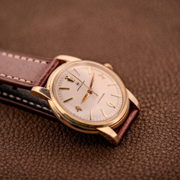 Hamilton Automatic Cal. 689 Sunburst Dial wristwatch with a 10k gold filled case and brown leather strap, displayed on a textured brown surface.