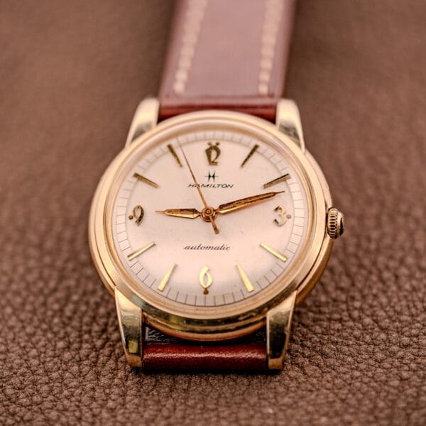 Hamilton Automatic Cal. 689 with a sunburst dial and 10k gold filled case, paired with a brown leather strap, displayed on a textured brown surface.