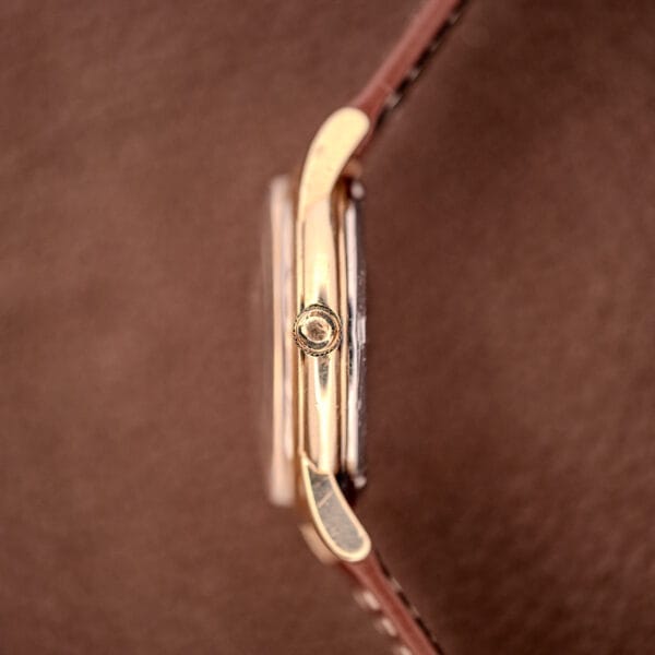 Side view of a Hamilton Automatic Cal. 689 with a sunburst dial, 10k gold filled case, and brown leather strap on a brown background.