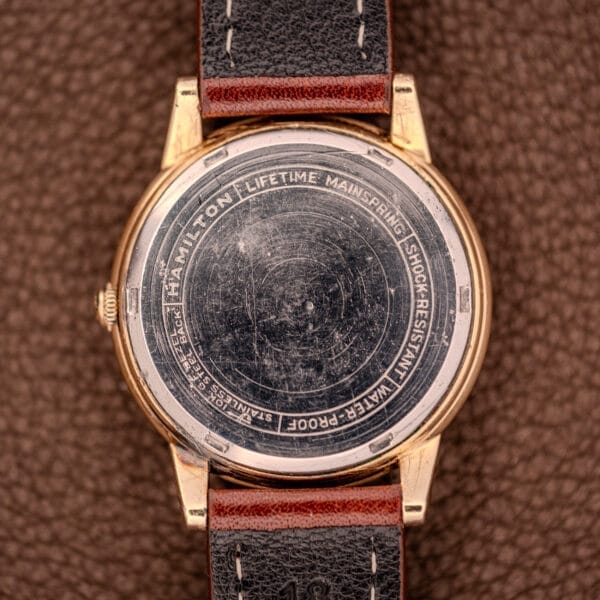 Back of a Hamilton Automatic Cal. 689 Sunburst Dial with worn engravings on a brown textured surface, showcasing its elegant 10k gold filled case.
