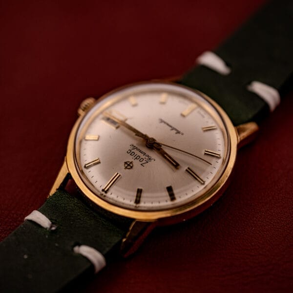 A Zodiac Hermetic Date Sunburst Dial Ref. 723-917 Automatic Cal. 70-72 wristwatch with a white face and black leather strap rests elegantly on a red surface.