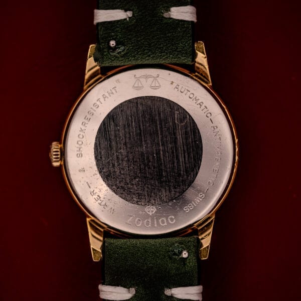 Back of a Zodiac Hermetic Date Sunburst Dial Ref. 723-917 Automatic Cal. 70-72 wristwatch with green strap, engraved metallic case, and center scratches.