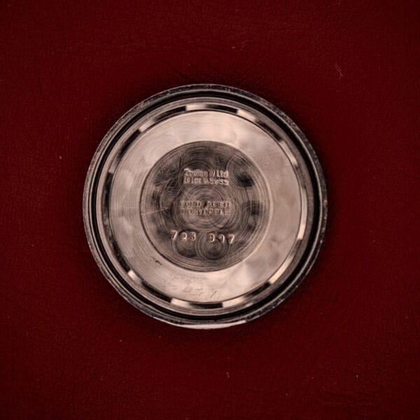 A round metal case back from the Zodiac Hermetic Date Sunburst Dial Ref. 723-917 Automatic Cal. 70-72, engraved with text, is shown on a red leather surface.