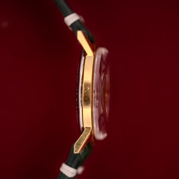 Side view of the Zodiac Hermetic Date Sunburst Dial Ref. 723-917 Automatic Cal. 70-72 gold wristwatch with black strap and sunburst dial, set against a deep red background.