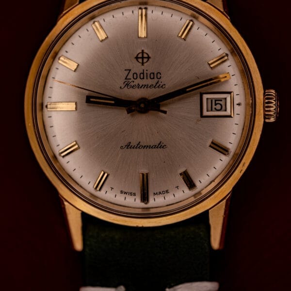A close-up of a Zodiac Hermetic Date Sunburst Dial Ref. 723-917 wristwatch featuring a gold case, automatic Cal. 70-72 movement, sunburst dial, and date display.