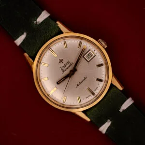 Zodiac Hermetic Date Sunburst Dial Ref. 723-917 wristwatch with green strap, sunburst silver dial, Automatic Cal. 70-72 movement, and date display, shown on a red background.