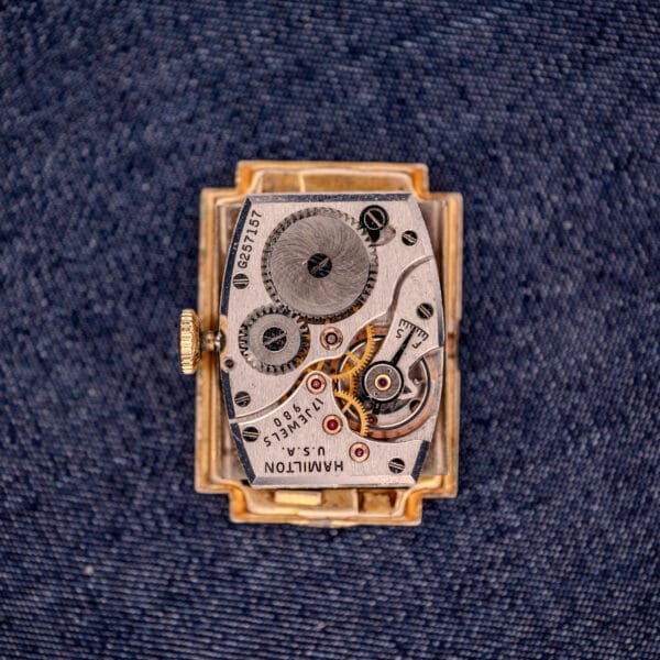 Close-up of a Hamilton Willshire 14k Gold Filled Art Deco Case Cal. 980 watch movement displayed on blue denim fabric.