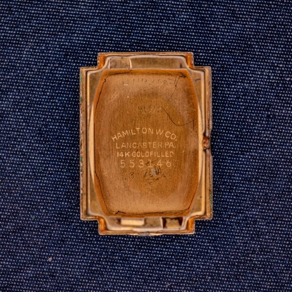 The Hamilton Willshire 14k Gold Filled Art Deco Case Cal. 980's engraved inside case back is shown on a blue fabric background.