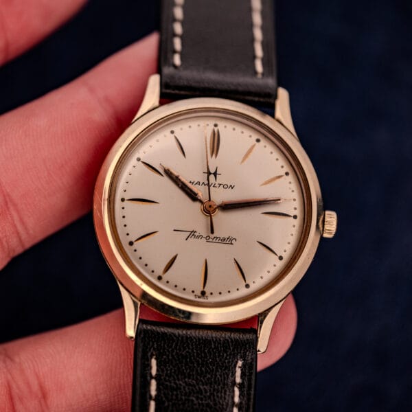 A hand holds a 1962 Hamilton Thin-o-Matic Cal. 663 with a black leather strap and a 10K Gold Filled case.