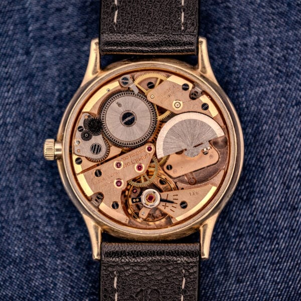 A close-up of the 1962 Hamilton Thin-o-Matic Cal. 663 10K Gold Filled watch movement, showcasing its visible gears and components against a blue fabric background.