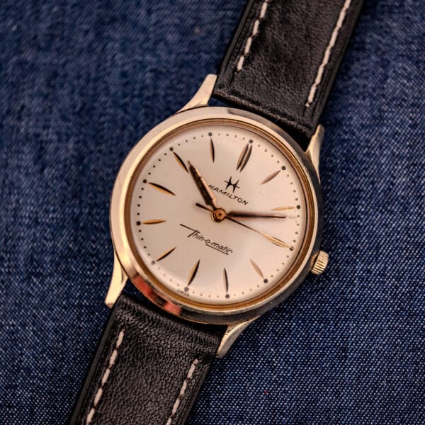 A 1962 Hamilton Thin-o-Matic Cal. 663 watch with a 10K Gold Filled case and black leather strap, shown on blue denim fabric.