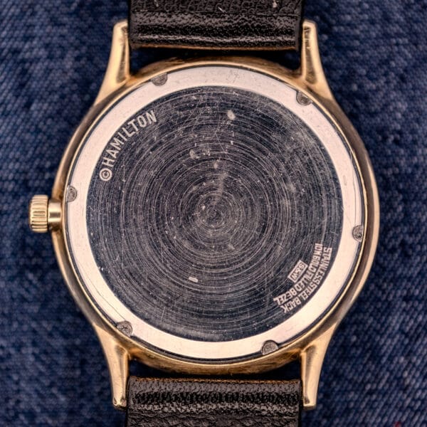 A scratched 1962 Hamilton Thin-o-Matic Cal. 663 10K Gold Filled watch with a leather strap rests on blue denim fabric.