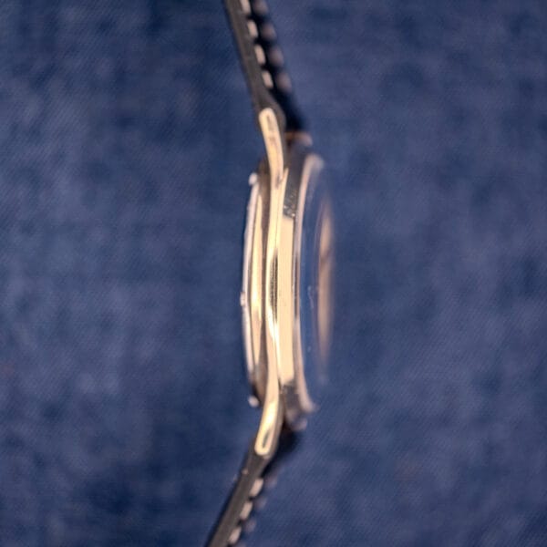 Side view of a 1962 Hamilton Thin-o-Matic Cal. 663 10K Gold Filled wristwatch with a black strap, photographed against a blue textured background.