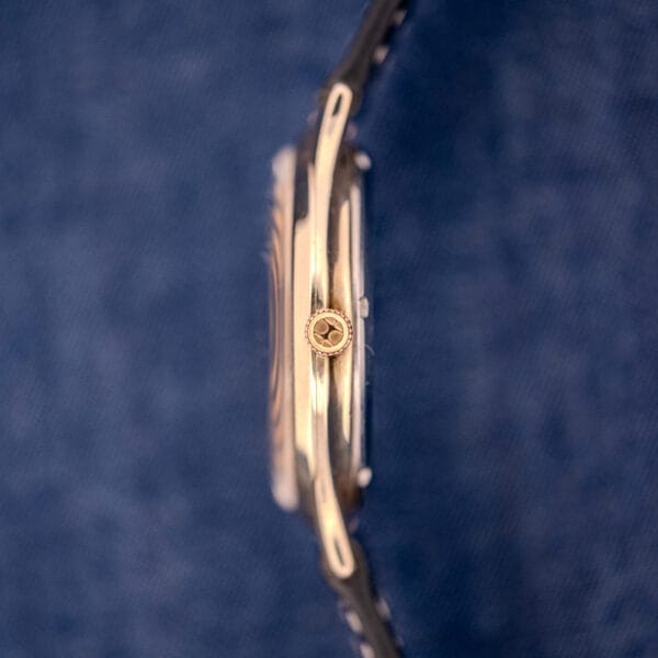 Side view of a 1962 Hamilton Thin-o-Matic Cal. 663 10K Gold Filled watch with crown, displayed on a textured blue background.