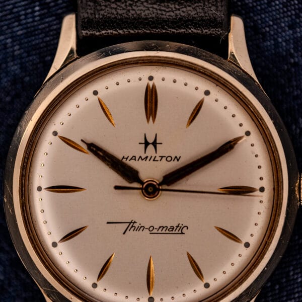 Close-up of a 1962 Hamilton Thin-o-Matic Cal. 663 wristwatch featuring gold markers, a 10K gold filled case, and a black leather strap.