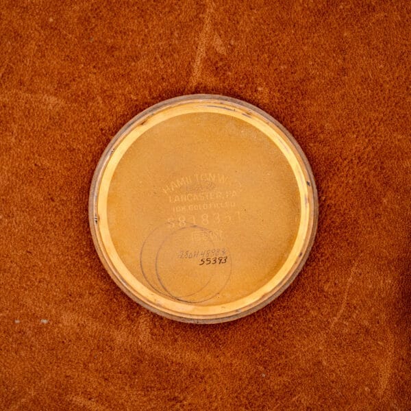 A 1966 Hamilton Thin-o-matic Cal. 668 10K Gold Filled watch back rests on brown suede, showing engraved text and numbers.