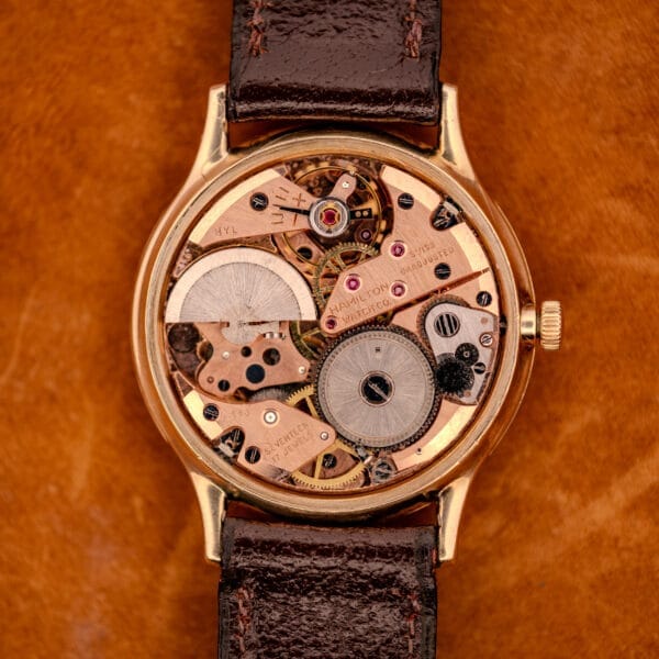 A close-up of the 1966 Hamilton Thin-o-matic Cal. 668 10K Gold Filled wristwatch showcasing its exposed mechanical movement and brown leather strap.
