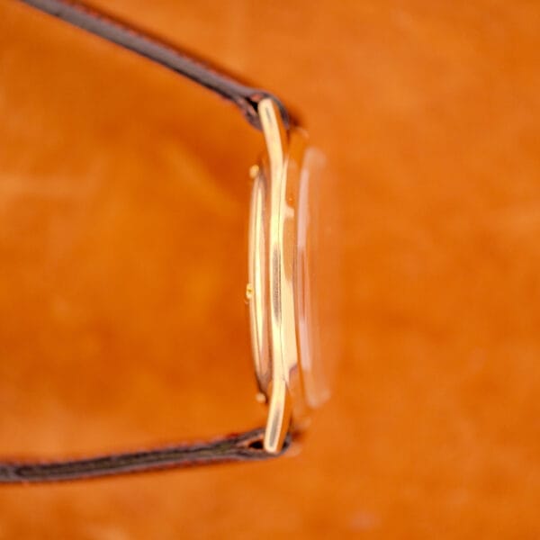 Side view of a 1966 Hamilton Thin-o-matic Cal. 668 10K Gold Filled wristwatch with a brown leather strap on an orange background.