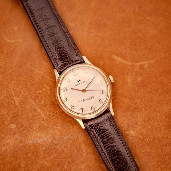 A 1966 Hamilton Thin-o-matic Cal. 668 with a brown leather strap and 10K gold filled case rests elegantly on a tan leather surface.