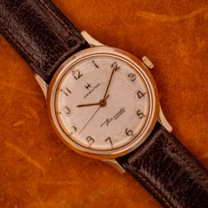 A 1966 Hamilton Thin-o-matic Cal. 668 10K Gold Filled wristwatch with a brown leather strap rests elegantly on a brown surface.