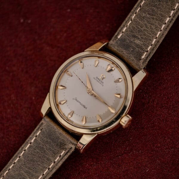 An Omega Automatic Seamaster Ref. 2846-2848 "Deluxe" with a gold capped case and leather strap, showcased on a red textured background.