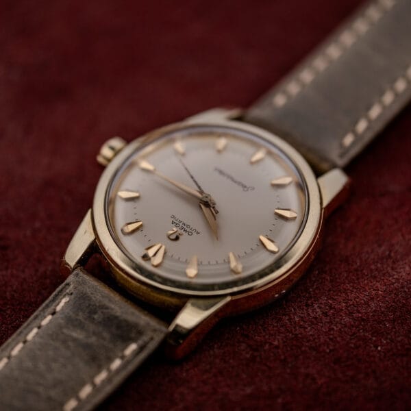 An Omega Automatic Seamaster Ref. 2846-2848 "Deluxe" with a gold capped case and leather strap is displayed on a burgundy fabric background.