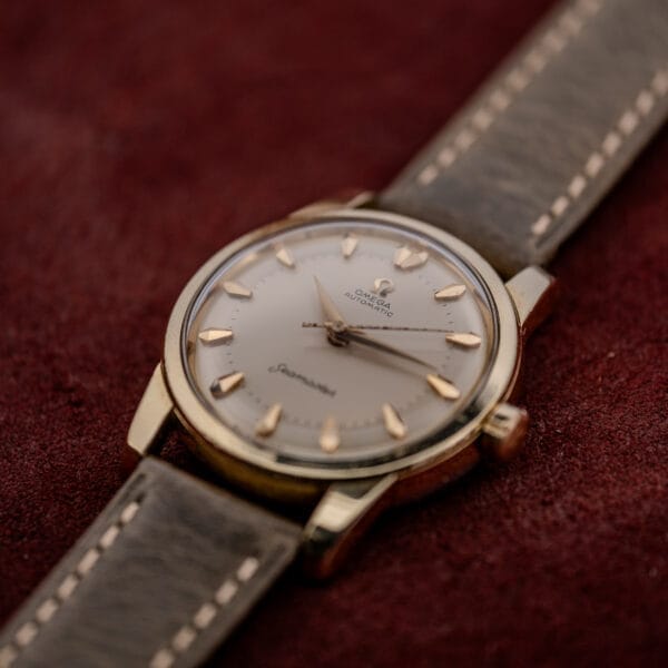 An Omega Automatic Seamaster Ref. 2846-2848 "Deluxe" with a gold capped case and leather strap is displayed elegantly on a red velvet surface.